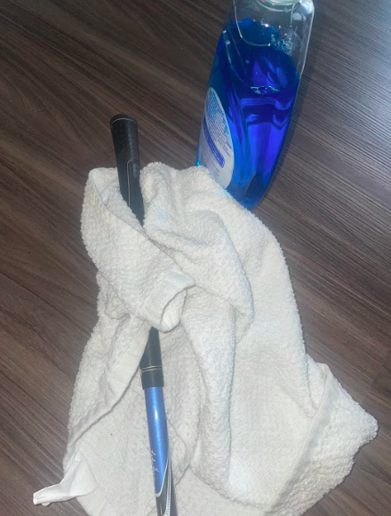 The upper half of a golf club wrapped in a towel sitting beside a bottle of dishsoap..