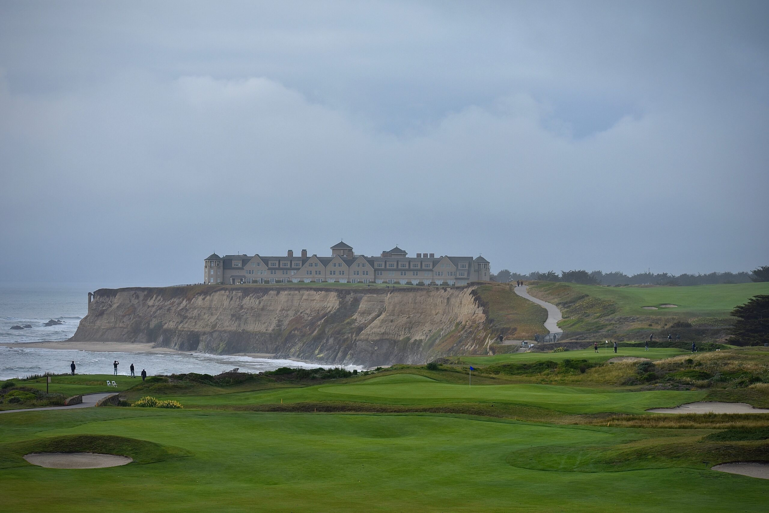 A sweeping golf course along the edge of a cliff with a gray sky in the background.