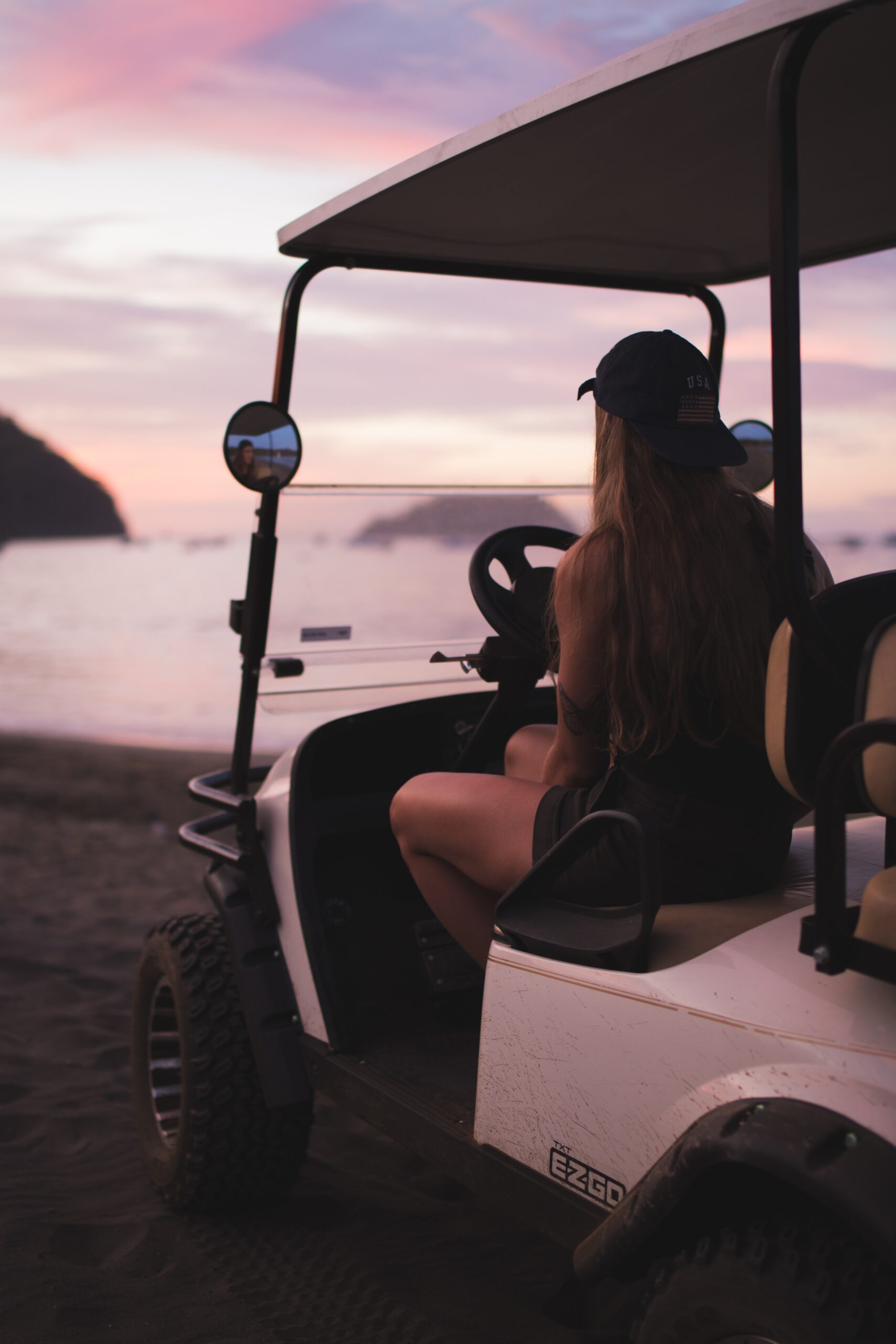 A woman sitting in a golf cart with a beautiful sky in the background.