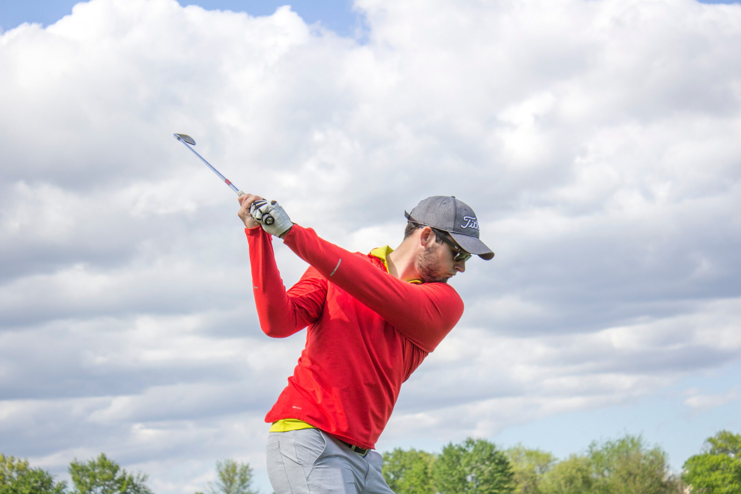 a golfer in a red shirt in the middle of his backswing.