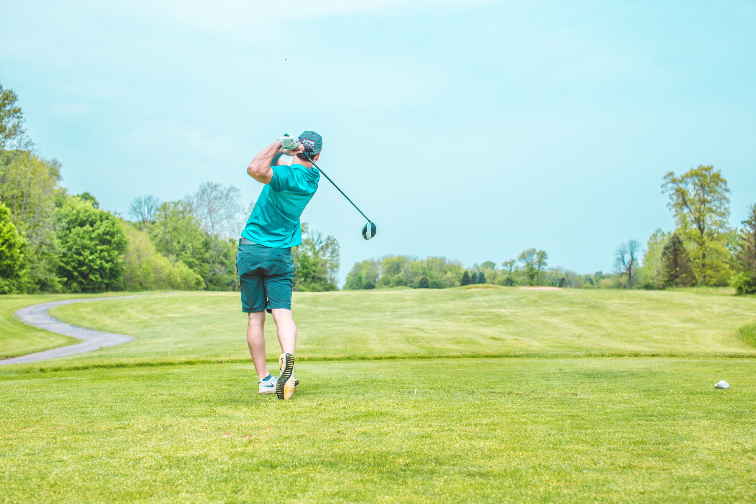 A golfer dressed in blue hitting a golf ball down a fairway.