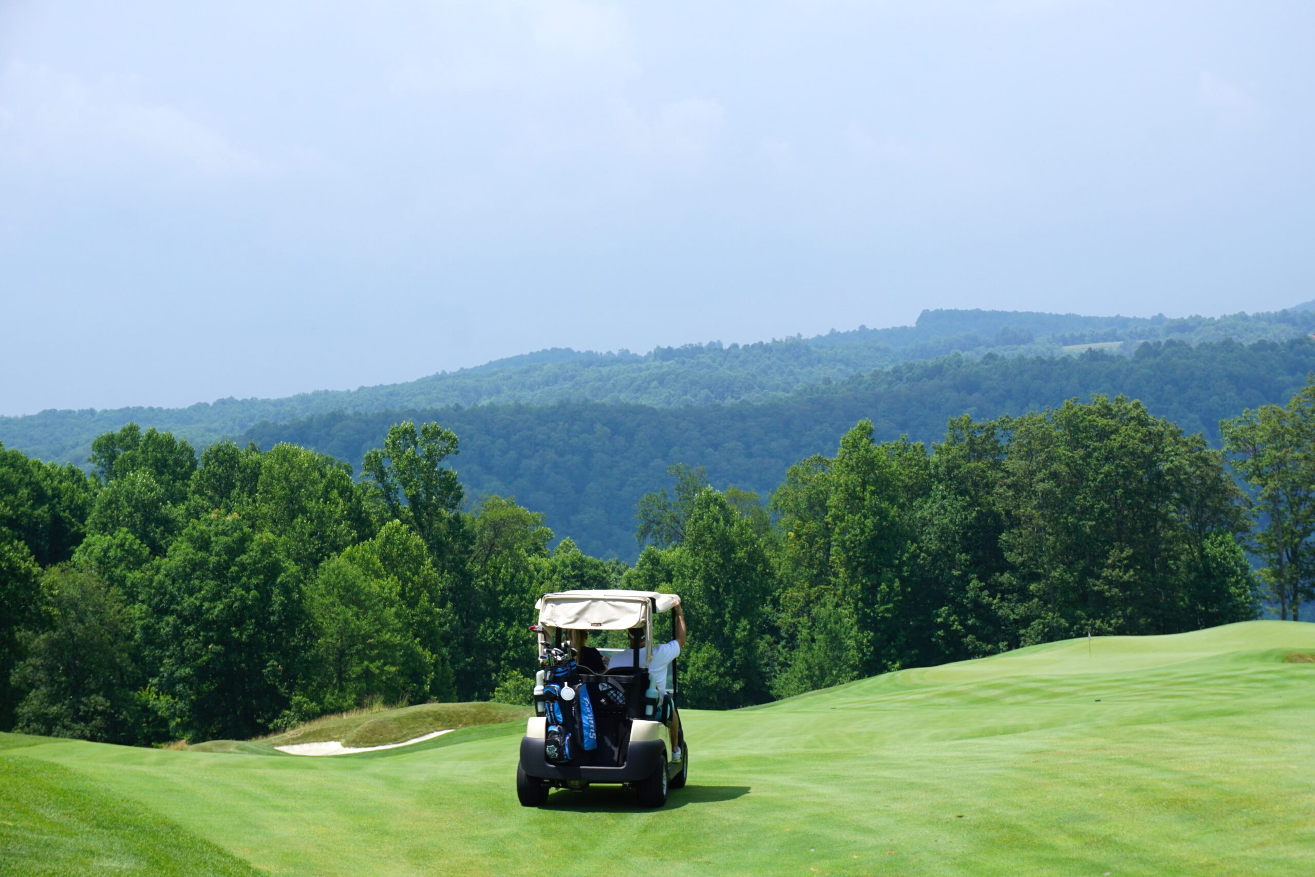 Wide shot of a rolling golf course with a golf car sitting on the fairway.