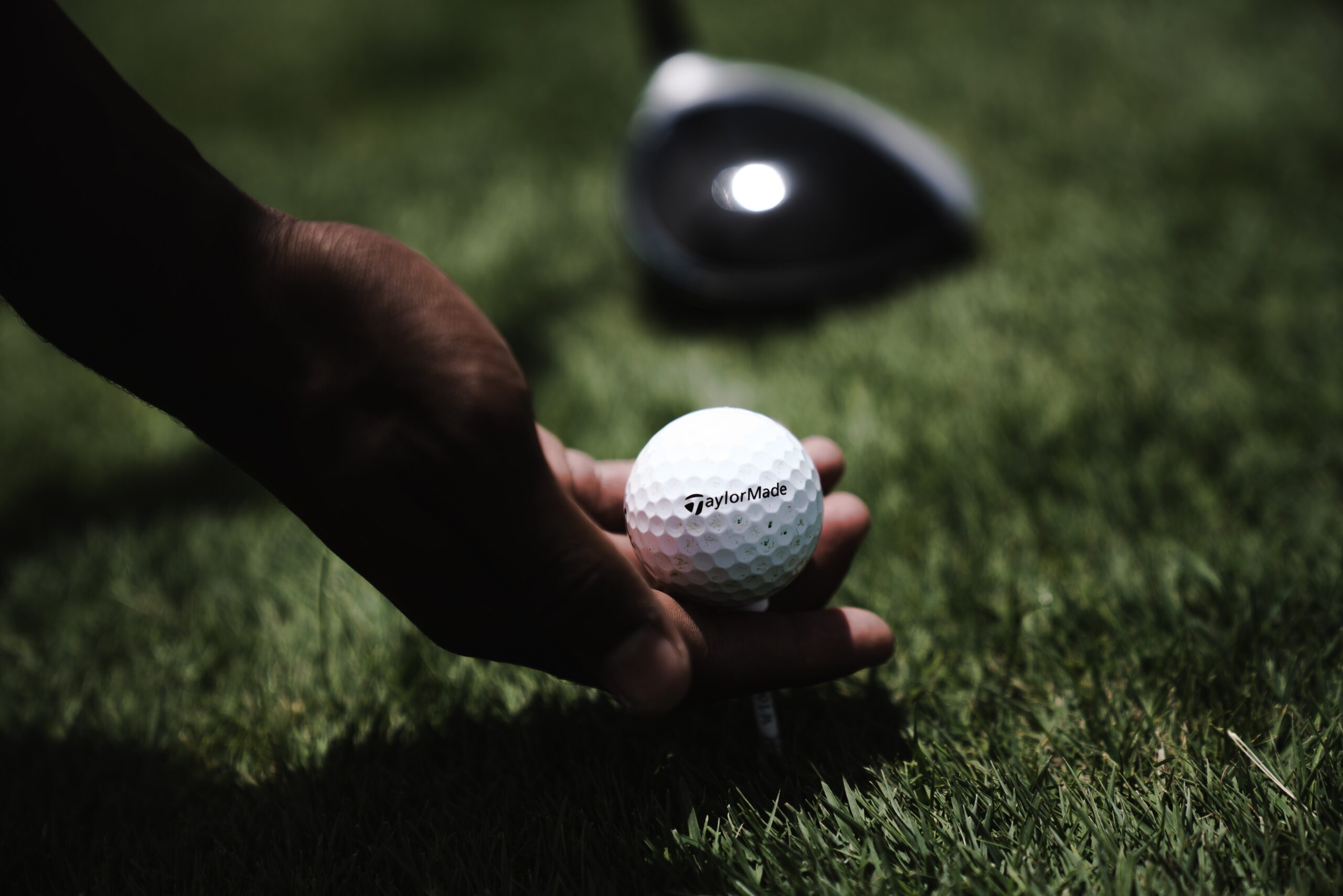 Close up of someone teeing up a ball with a driver head in the background.