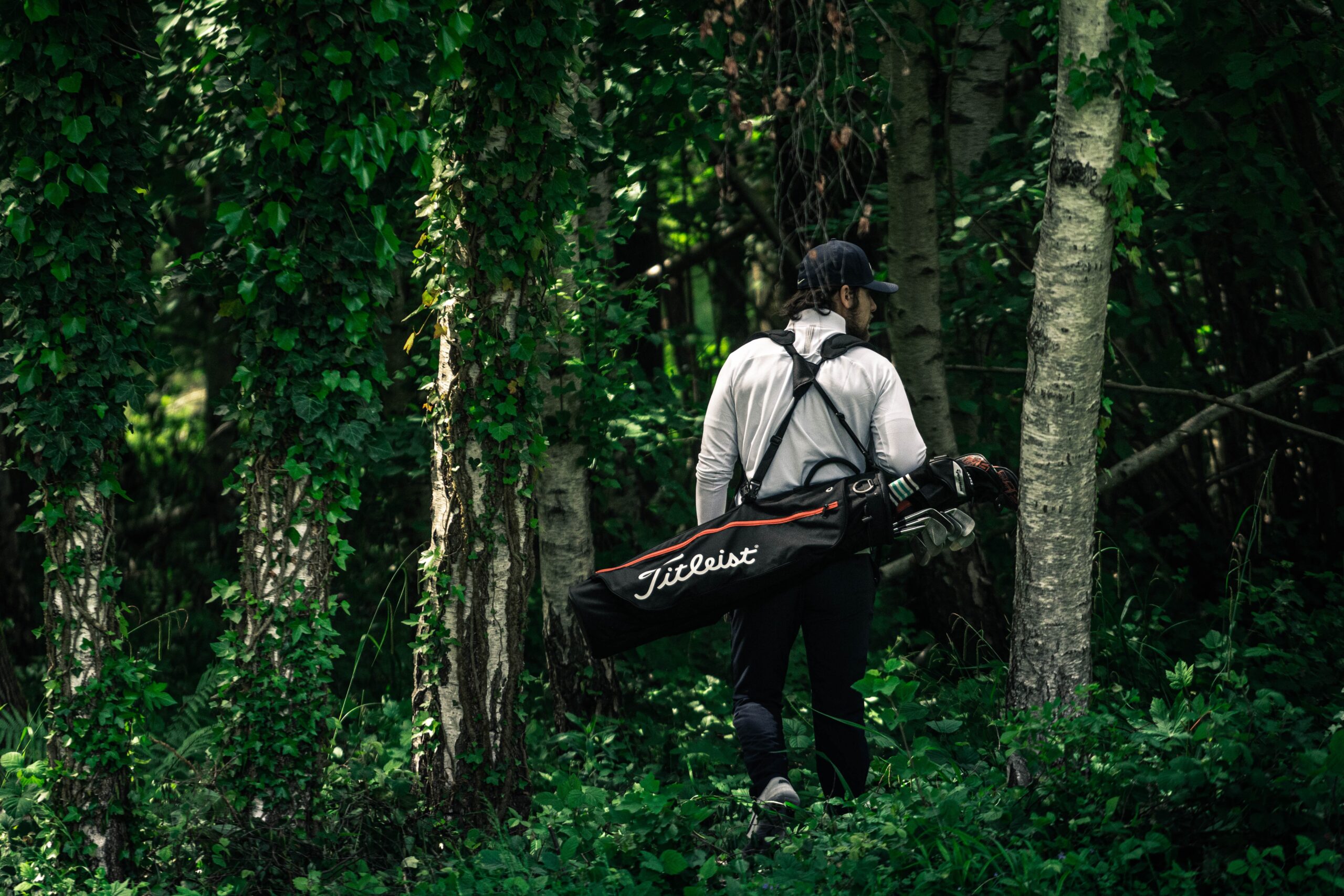 A golfer with his golf bag slung across his back walking through the woods.