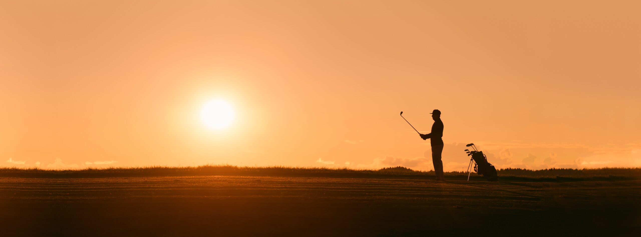 A wide shot of a silhouette of a golfer in front of a sunset.