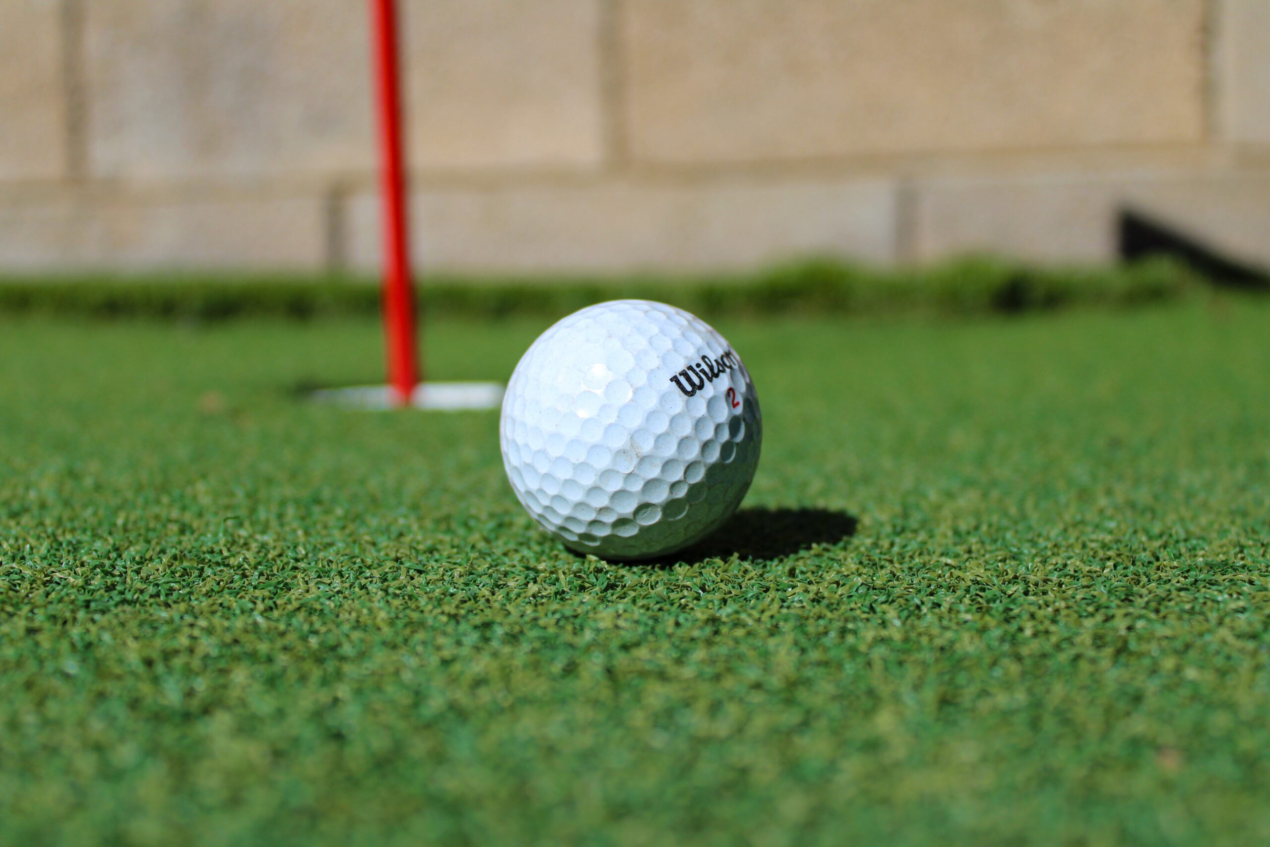 Close up of a golf ball on a putting green with a pin and hole in the background.