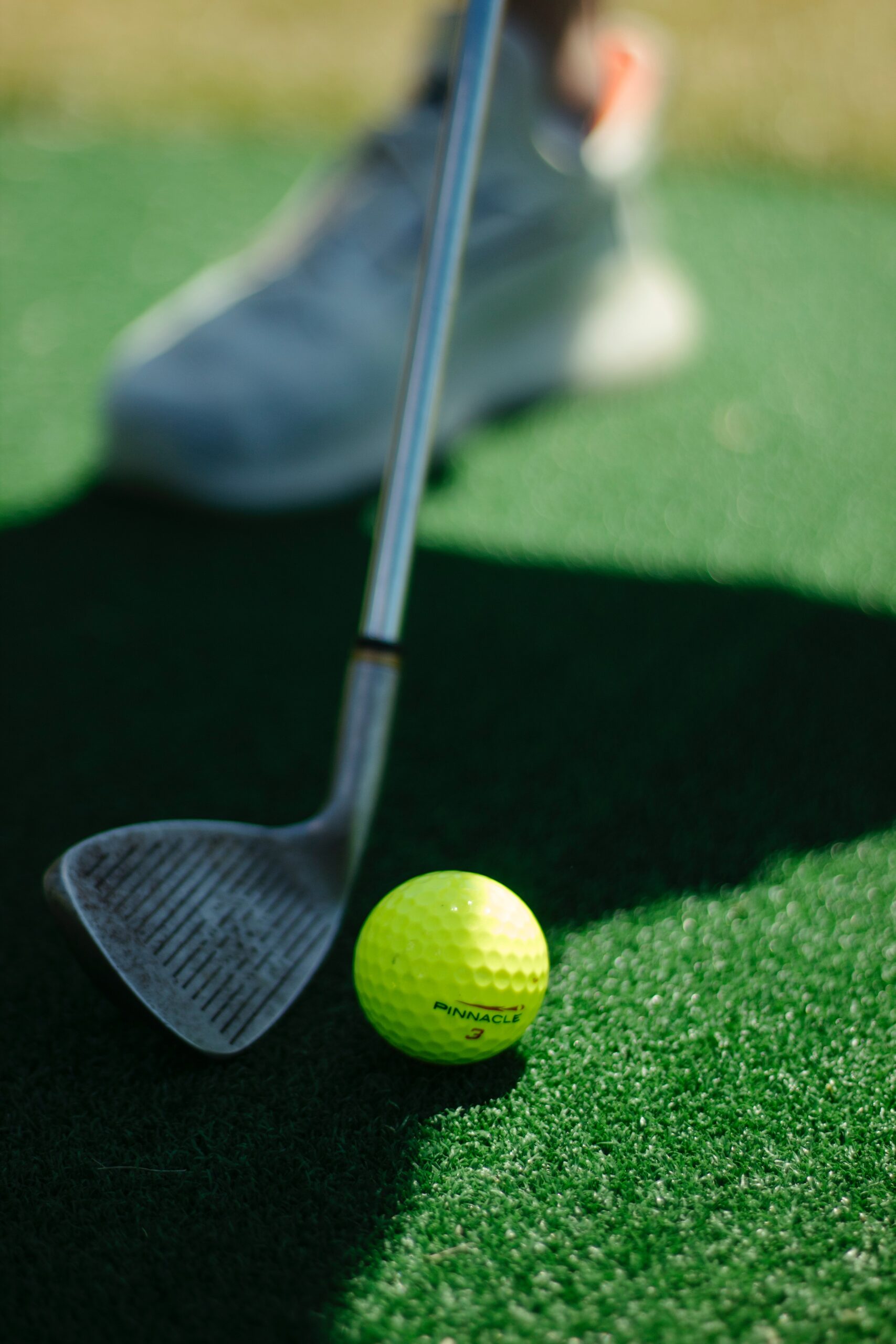 Close up of a golf iron resting behind a neon yellow golf ball.