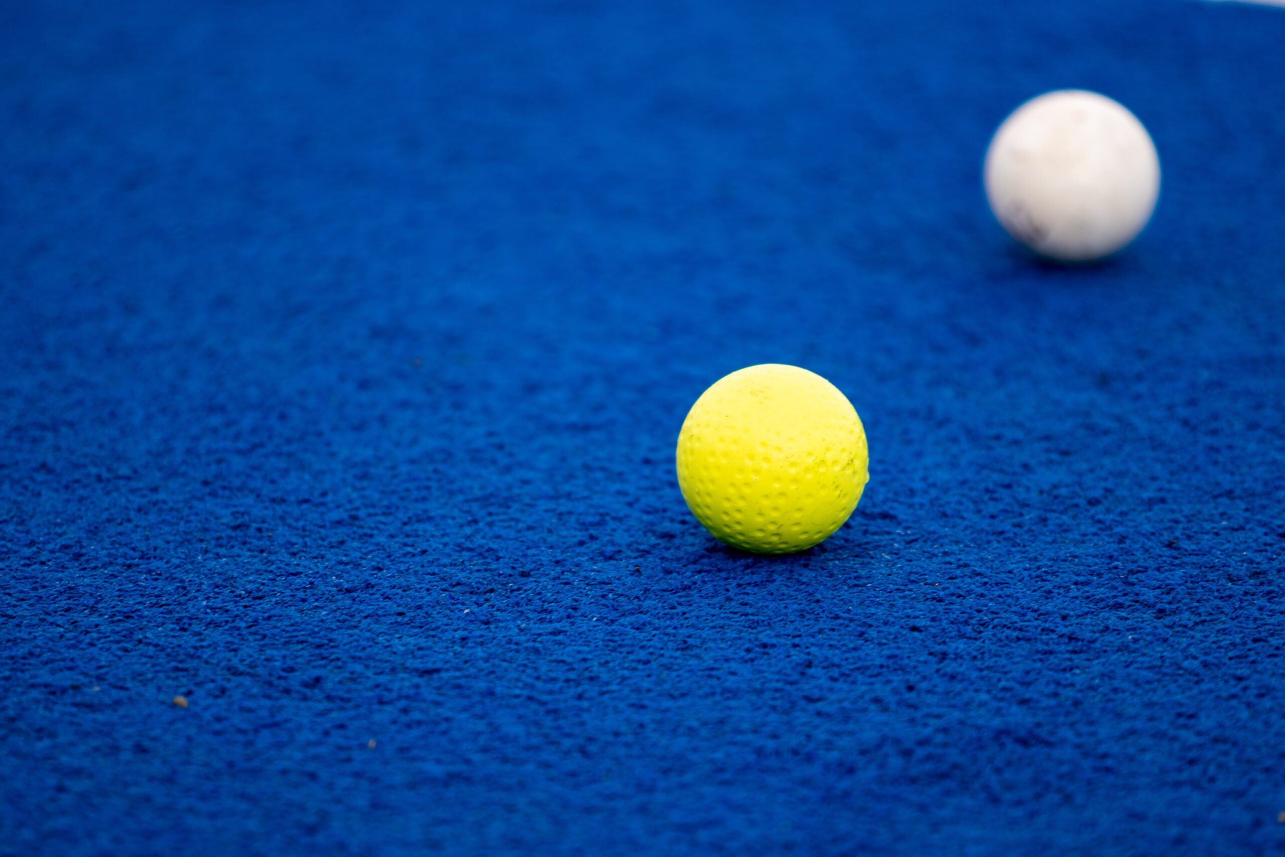 A yellow and white golf ball sitting on blue turf.