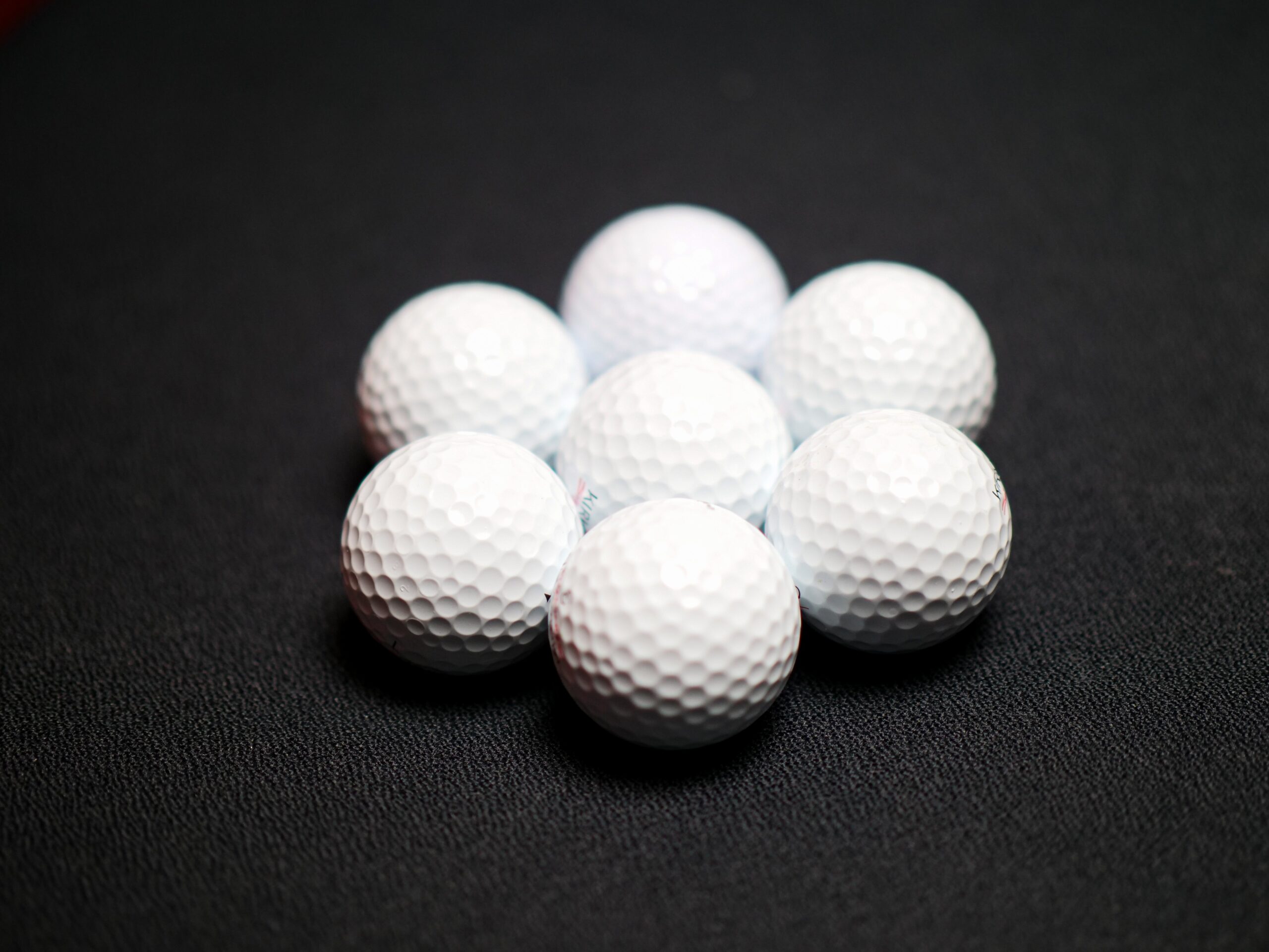 Seven golf balls gathered together in a hexagon shape on a black surface.