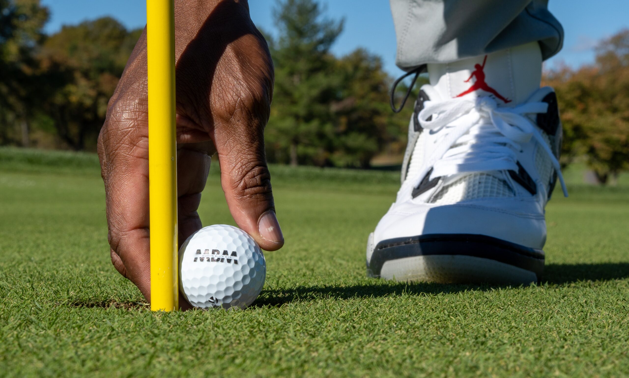 A golfer wearing Jordan golf shoes reaching down to retrieve a ball from a hole.