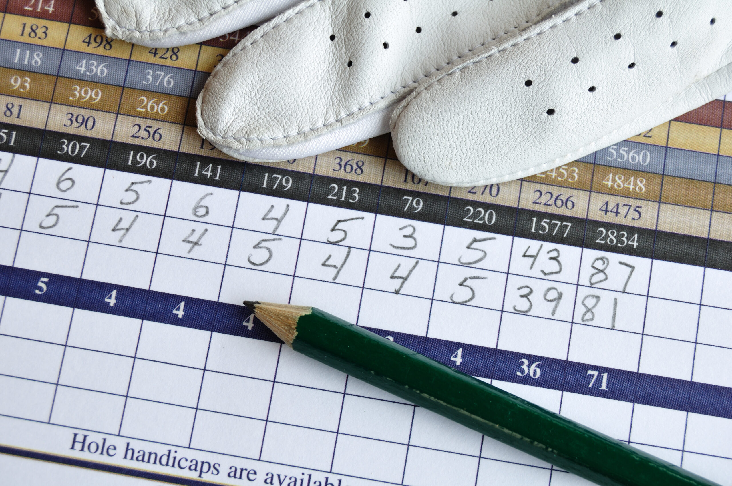 A golf scorecard with a pencil and golf glove in frame.