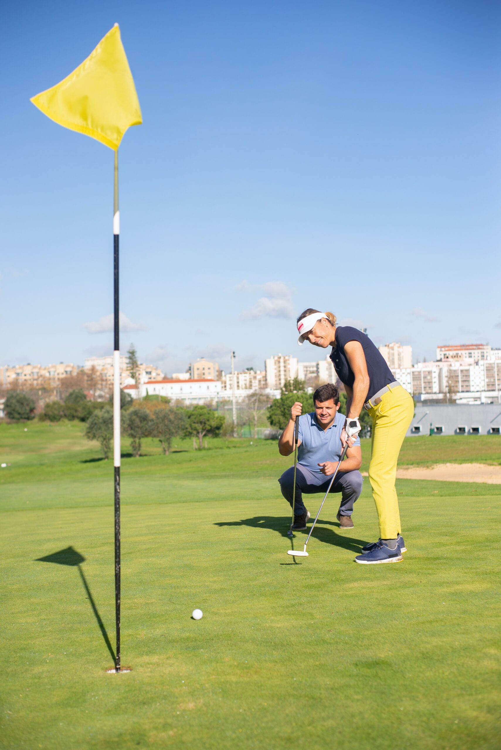 Two golfers watching a golf ball rolling towards the hole on a green.